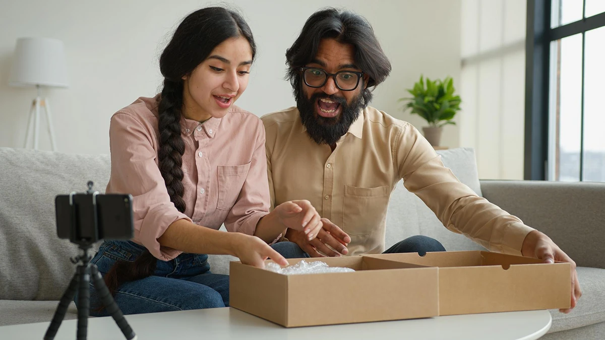 Two people happily unboxing a package while filming on a smartphone