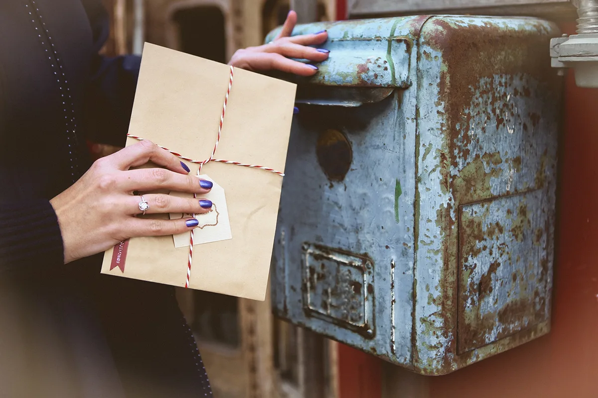A person sending a direct mail package into an old blue mailbox