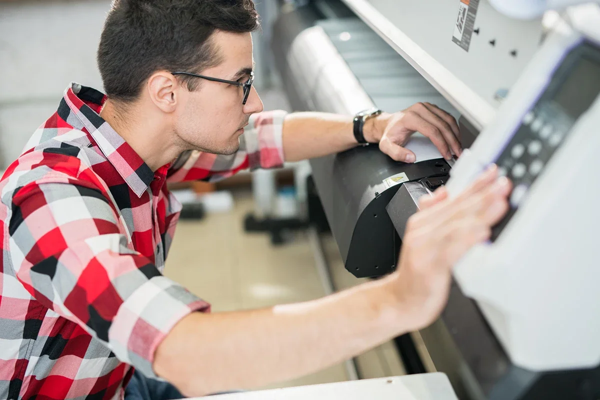 A technician operating a large-format printer in a print shop
