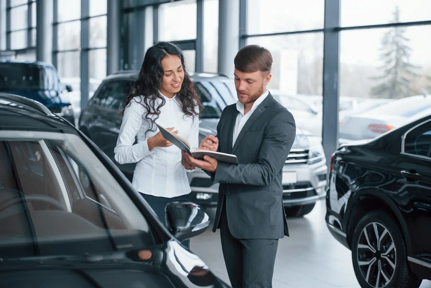 Car dealership salesperson assisting a customer while reviewing vehicle options in the showroom