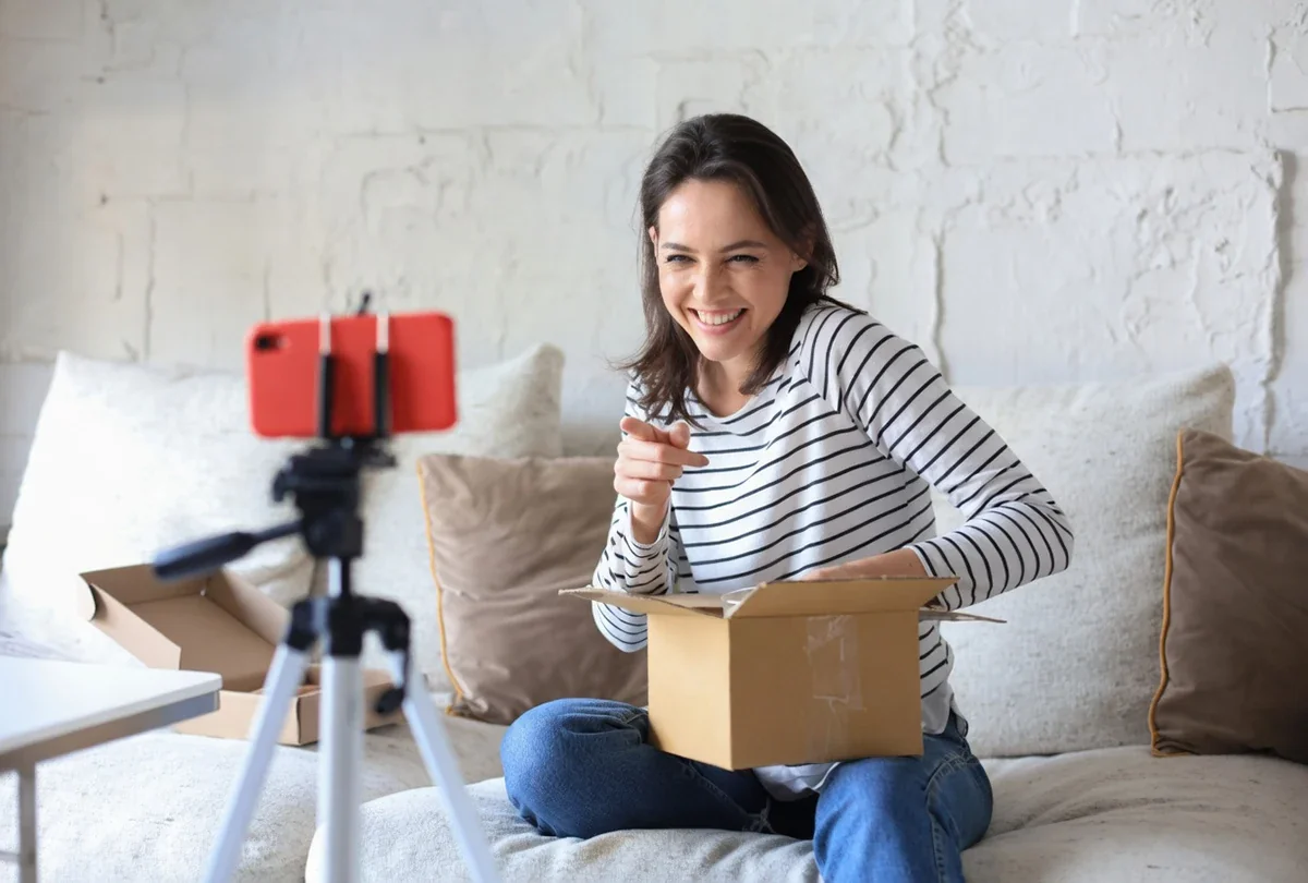 Female social media influencer smiling while opening a branded box on camera during an unboxing video shoot