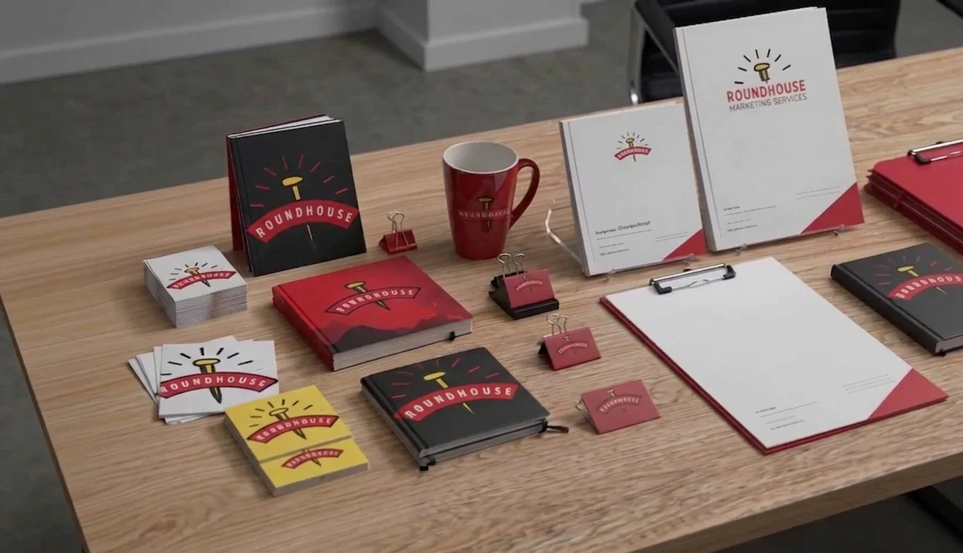Roundhouse Partners branded print collateral and promotional products, including notebooks, business cards, mugs, and stationery in brand colors