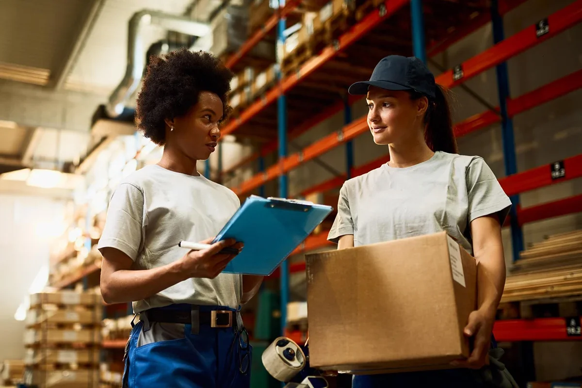 Two warehouse staff reviewing a shipment checklist inside a fulfillment warehouse.