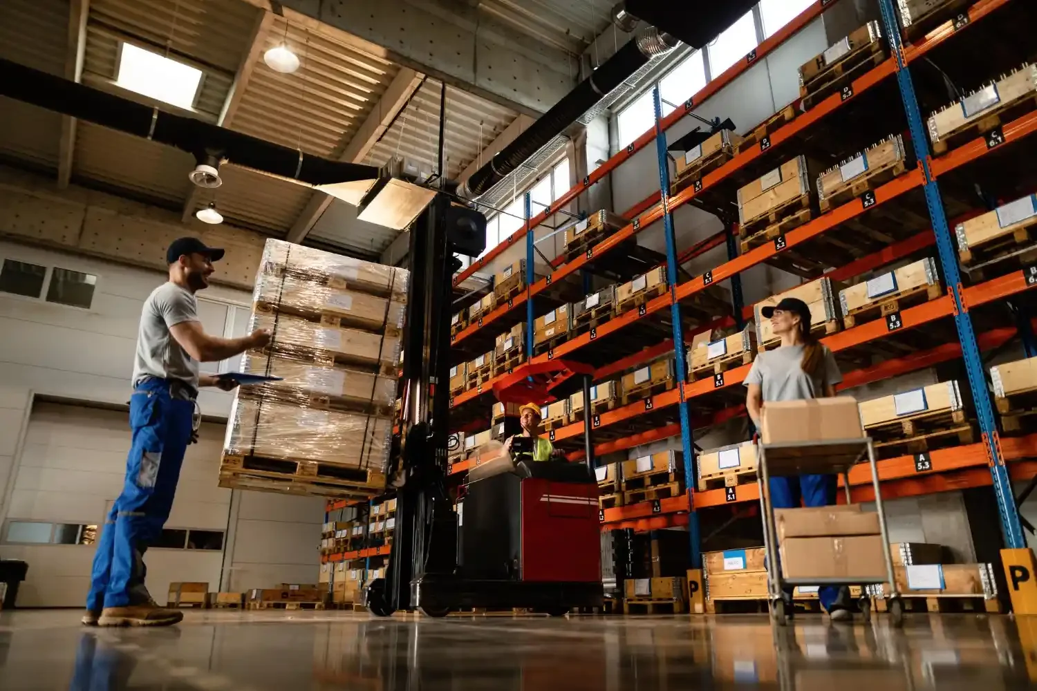 Warehouse workers moving boxed inventory and pallets through a large storage facility